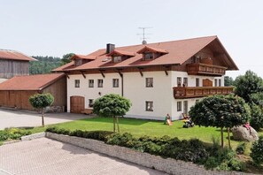 A large two-story house with a sloped roof, a balcony, and a well-maintained lawn with trimmed trees.