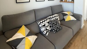Una sala de estar moderna con un sofá gris, cojines estampados y cuadros en la pared.
