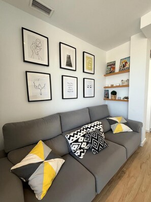 Ein modernes Wohnzimmer mit einem grauen Sofa, gemusterten Kissen und gerahmten Bildern an der Wand.