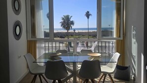 Un comedor con una mesa y sillas de vidrio, vista a la playa y dos espejos decorativos colgados en la pared.