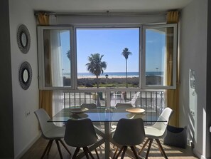 Ein Essbereich mit einem Glastisch und Stühlen, Blick auf den Strand und zwei dekorative Wandspiegel.