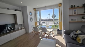 Una sala de estar moderna con un televisor de pantalla plana, una mesa de comedor de vidrio y un sofá con cojines estampados.