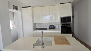 Una cocina moderna con armarios blancos, un lavamanos de acero inoxidable, un microondas y un horno.