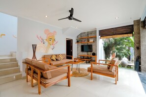 A modern living room with a sofa set, a coffee table, and a TV. There is a staircase leading to another level. - VILLA NARADA -TROPICAL PARADISE VILLA - PRIVATE POOL - CONVENIENT LOCATION (seminyak)