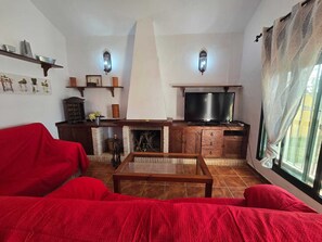 Ein Wohnzimmer mit einem roten Sofa, einem Kamin, einem Fernseher und einem Fenster mit Vorhängen.