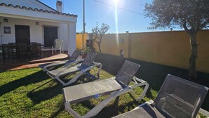 En uteplats med solstolar, en grill och ett matbord, placerat utanför ett hus.