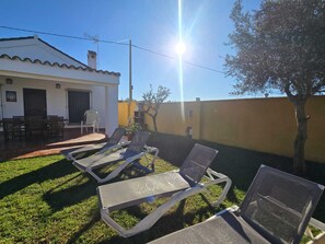 Eine Terrasse mit Liegestühlen, einem Grill und einem Esstisch vor einem Haus.