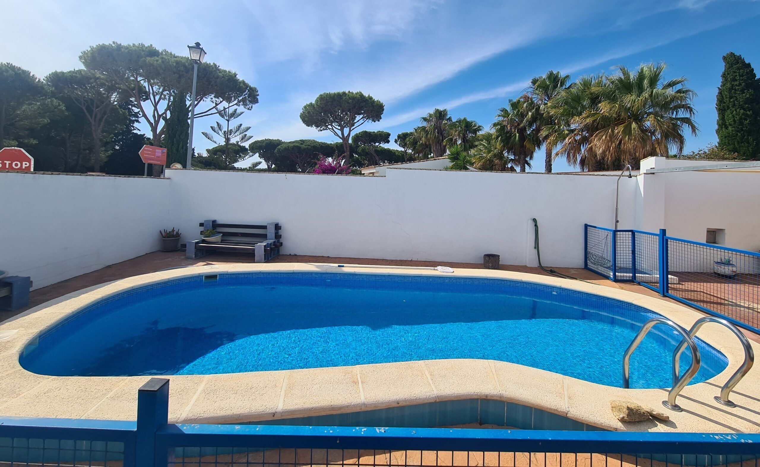 A swimming pool with a blue border, a bench, and a stop sign in the background.