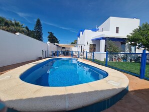Ein Pool mit geschwungener Kante, umgeben von einem blauen Zaun, neben einem weißen Gebäude mit blauen Akzenten.