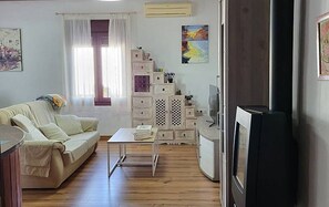 Ein Wohnzimmer mit einer Couch, einem kleinen Tisch, einem Fernseher und einer Kommode mit Schubladen.