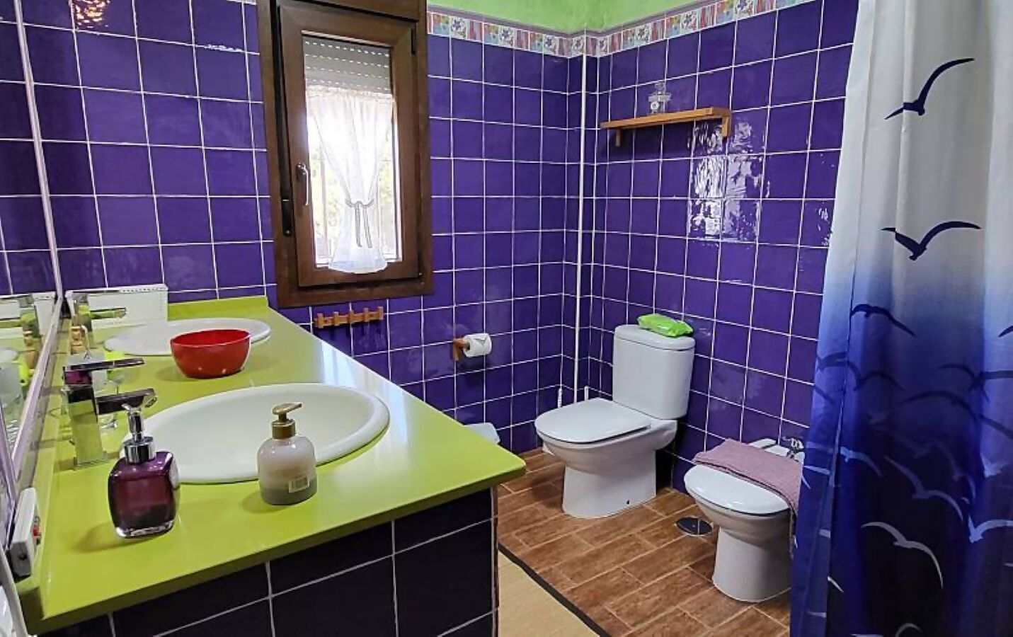 A bathroom with a green sink, a white toilet, and a purple tiled wall.