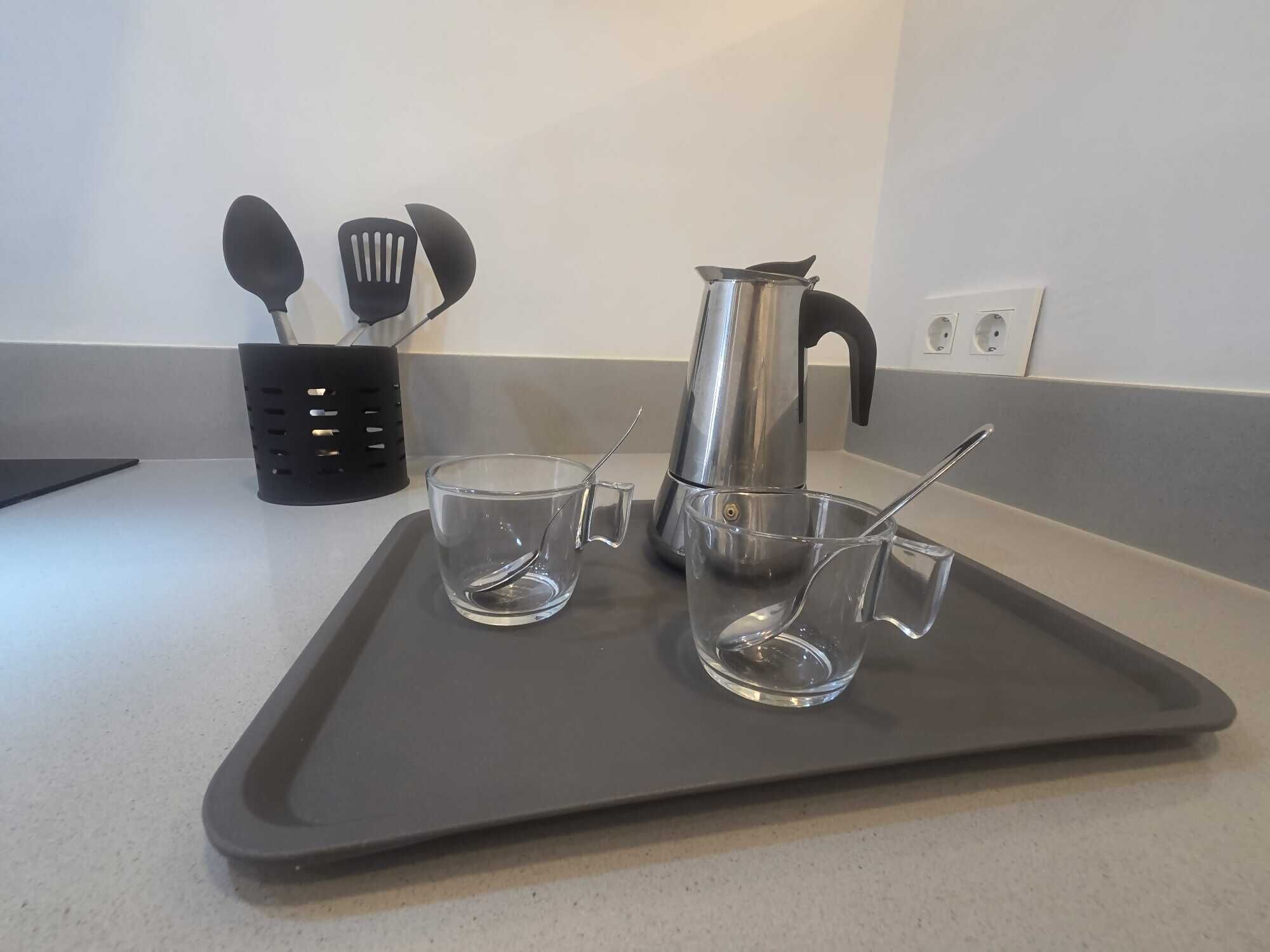 A kitchen counter with a tray holding two clear glasses and a stainless steel kettle.