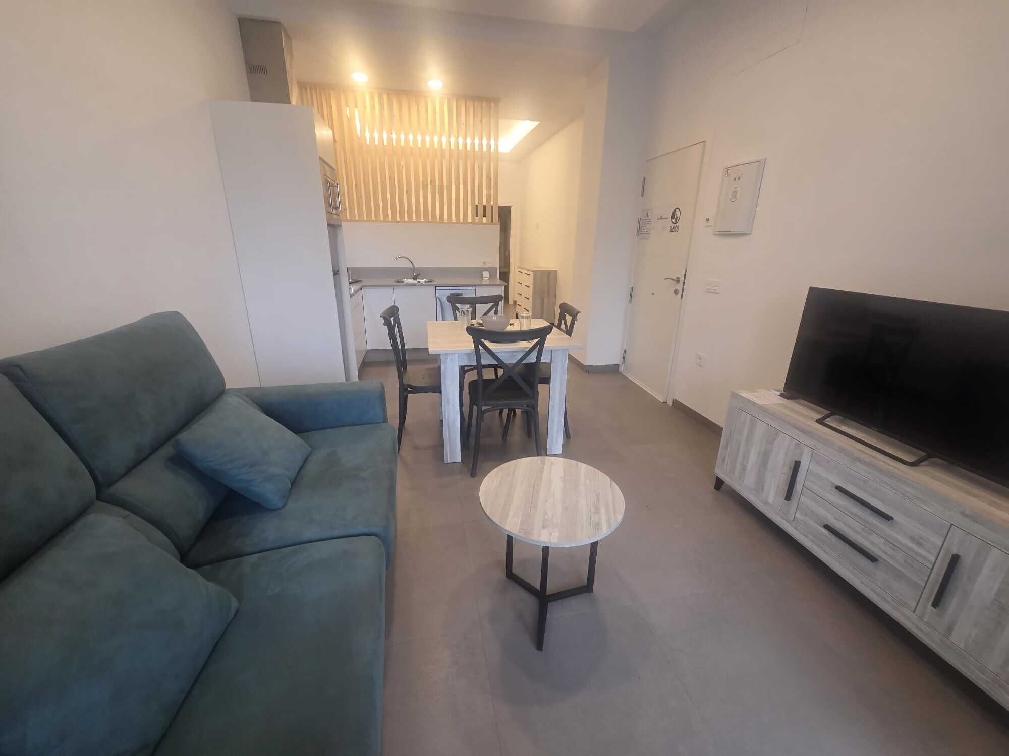 Un salon moderne avec un canapé, un téléviseur, une table à manger avec des chaises, et une cuisine en arrière-plan.