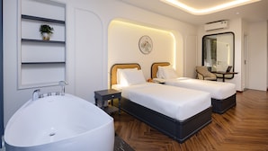 Una habitación de hotel con una bañera grande, dos camas individuales, una mesita con una computadora portátil, una silla y un aire acondicionado instalado en la pared.