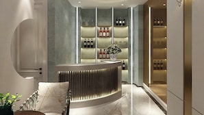 Un área de recepción moderna con un mostrador curvo, una exhibición de vinos y un espacio de descanso con cojines estampados.