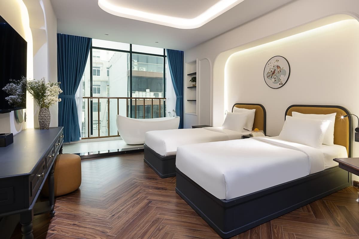 Une chambre d’hôtel avec deux lits, un bureau, une chaise, une télévision et une grande fenêtre donnant sur des immeubles.