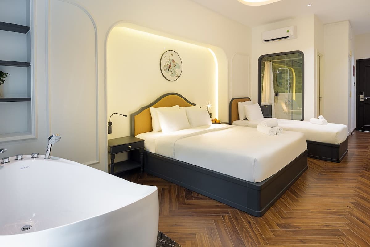 A modern hotel room with a large bathtub, two beds, a shower area, and a wall-mounted air conditioning unit.