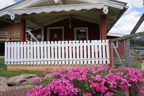 Ein Holzhaus mit weißem Zaun, einer Veranda und pinkfarbenen Blumen im Vordergrund.