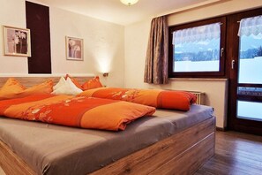 Ein Schlafzimmer mit einem Bett, Kissen, einem Fenster mit Vorhängen und gerahmten Bildern an der Wand.
