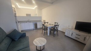 A modern living space with a sofa, a dining table with chairs, a TV, and a kitchen area with cabinets and a dishwasher. - Apartment 2 Virgen de la Luz (Conil De La Frontera)