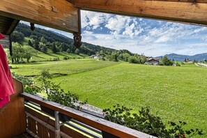Un balcon en bois offrant une vue sur un champ verdoyant et sur des maisons situées au loin.