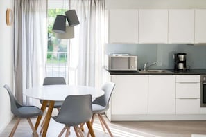 Eine moderne Küche mit weißen Schränken, einer Mikrowelle, einer Kaffeemaschine und einem Essbereich mit rundem Tisch und grauen Stühlen.