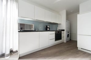 Eine moderne Küche mit weißen Schränken, einer Mikrowelle, einer Kaffeemaschine, einem Backofen und einer Waschmaschine.