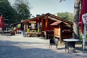 Ein rustikaler Außenbereich mit Tischen und Stühlen, einer Holzhütte mit einem Schild und einem roten Sonnenschirm.