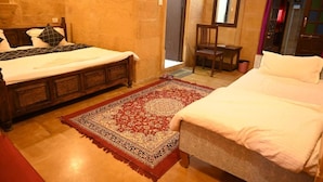 A room with two beds, a wooden chair, a red patterned rug, and a mirror on the wall. - hotel kalyan haveli jaisalmer (Jaisalmer)