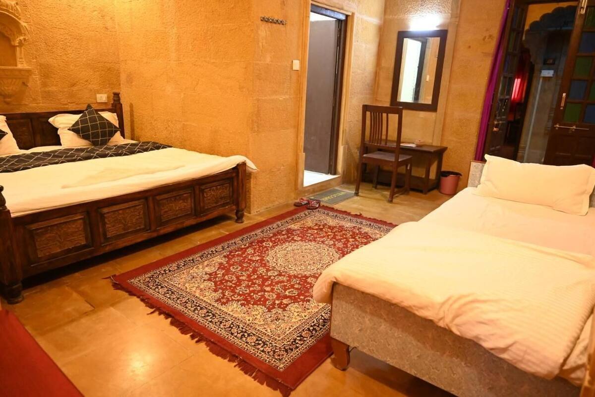 Ein Zimmer mit zwei Betten, einem Holzstuhl, einem roten Teppich mit Muster und einem Spiegel an der Wand.