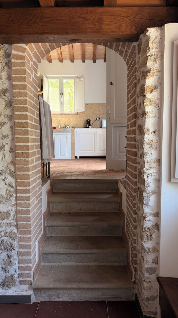 A stone staircase leading to a kitchen with white cabinets and a brick wall. - Absolute Relaxation, Total Isolation among the Olive Trees and Sea View (Camaiore)