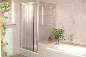 Ein Badezimmer mit Dusche, Badewanne, Handtuchhalter und einer Topfpflanze.