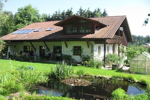 Ein Haus mit geneigtem Dach, einem Teich und einem Gewächshaus.