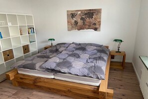 Un dormitorio con una cama de madera, un mapa mundial en la pared, una estantería y dos mesitas de noche.