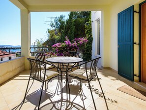 Ein Balkon mit rundem Tisch und Stühlen, Blick aufs Meer und eine Tür mit blauem Fensterladen.