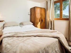 Uma cama com um cobertor macio, um guarda-roupa de madeira e uma janela com cortinas.