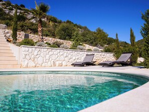 A swimming pool with clear water, a stone wall, and two lounge chairs. - Vacation home Nerium by Interhome (Trogir/Vranjica)