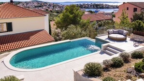 Ein Pool mit geschwungener Kante, eine Liege und eine Steintreppe, die zu einem Deck führt.