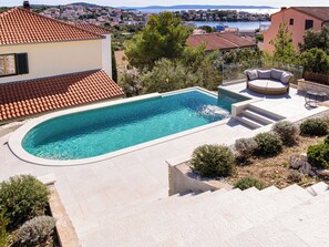 Ein Pool mit geschwungener Kante, eine Liege und eine Steintreppe, die zu einem Deck führt.