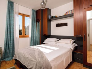 Ein Schlafzimmer mit einem Bett, Vorhängen, einem Fenster, einem Regal mit Büchern und einem Kleiderschrank.
