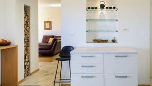 Eine moderne Küche mit weißer Arbeitsplatte, einer Glastrennwand mit Küchenutensilien und einem Essbereich mit braunem Ledersofa.