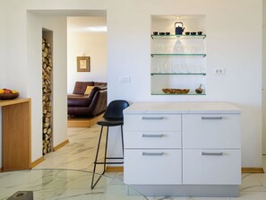 Eine moderne Küche mit weißer Arbeitsplatte, einer Glastrennwand mit Küchenutensilien und einem Essbereich mit braunem Ledersofa.