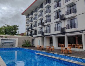 A hotel with a swimming pool, outdoor seating, and multiple balconies.