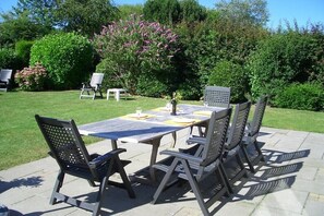 An outdoor patio with a table and chairs, surrounded by greenery and trees.