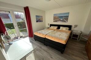 A bedroom with a bed, a desk, a chair, a mirror, and a view of the outdoors.