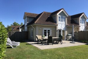 Une maison à deux étages avec un patio, une cour arrière clôturée et un ciel dégagé.