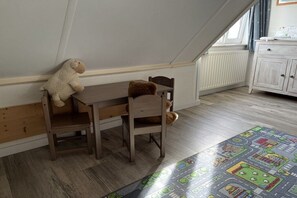 Una habitación con techo inclinado, una mesa de madera, dos sillas, un osito de peluche sobre la mesa, un armario y una alfombra estampada.