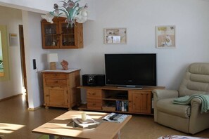 Ein Wohnzimmer mit Fernseher, Holzschränken, einer Couch und einem Tisch.
