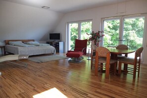 A bedroom with a bed, a TV, a red chair, a dining table with chairs, and large windows. - Holiday apartment with 1 bedroom (Tübingen)