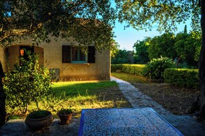 Un bâtiment rustique doté d’une fenêtre et d’une porte, entouré de verdure et bordé d’un chemin pavé.